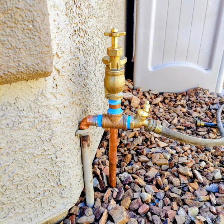 Small copper manifold with four outlets, connected to a valve beside an exterior house wall.