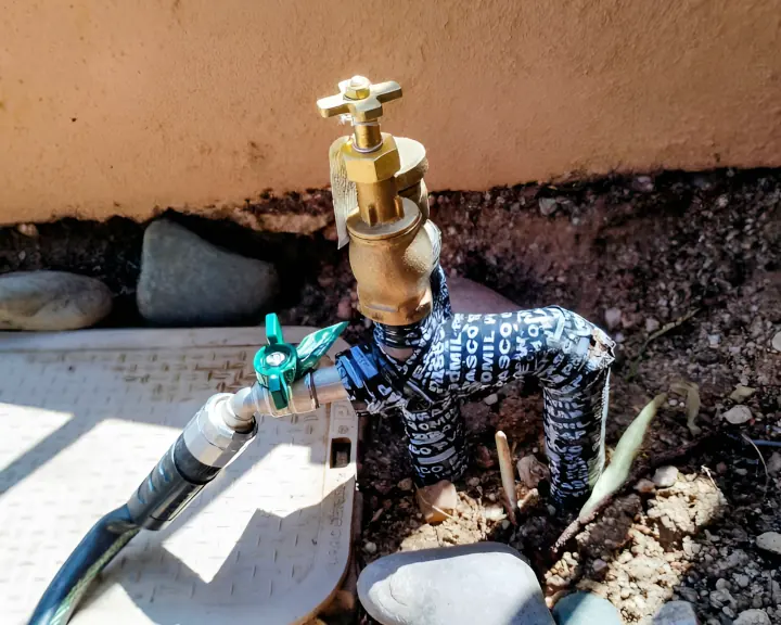 Brass outdoor faucet with insulated pipe wrapping and garden hose connection installed in Tucson Arizona landscape by professional irrigation company
