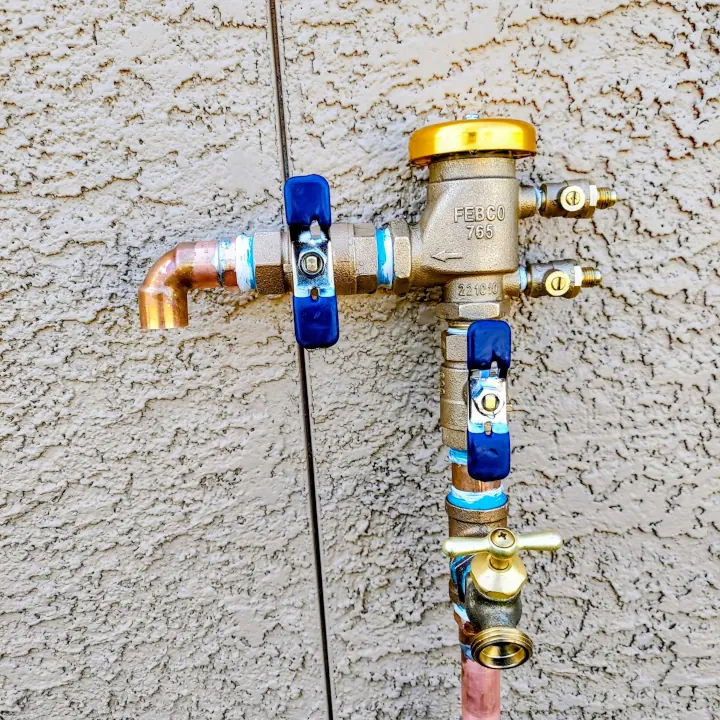Copper irrigation manifold with blue valves beside an exterior wall.